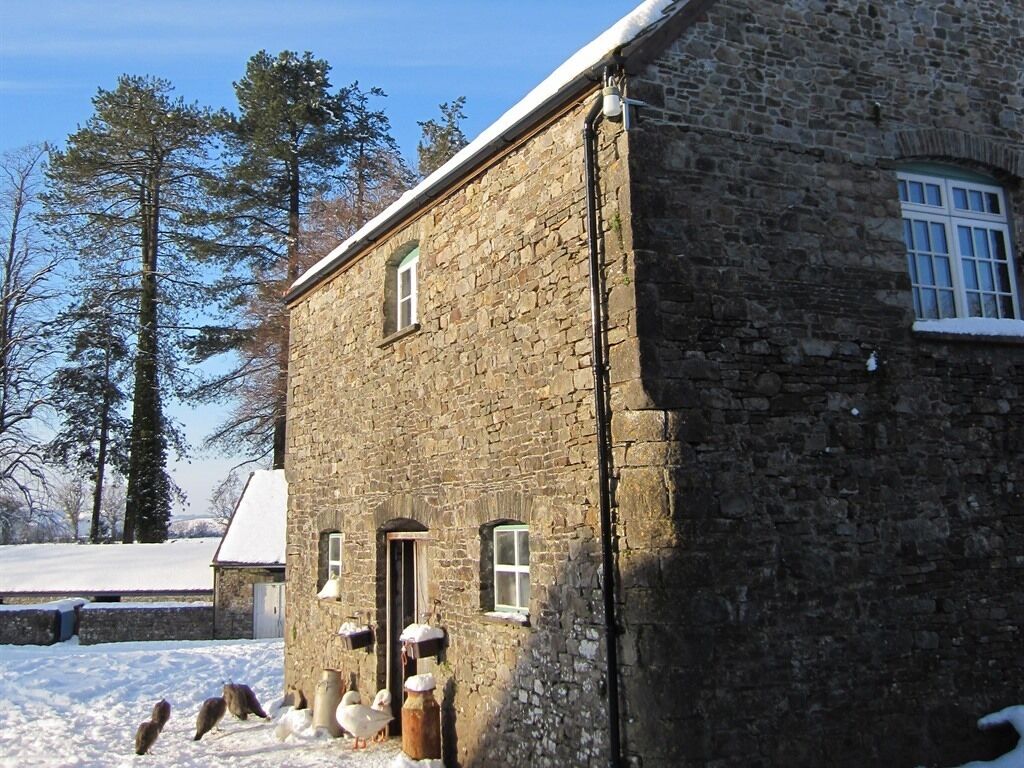 Un edificio de piedra con tejado nevado, una puerta pequeña y una ventana.