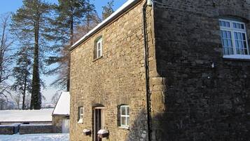 Un edificio de piedra con tejado nevado, una puerta pequeña y una ventana.
