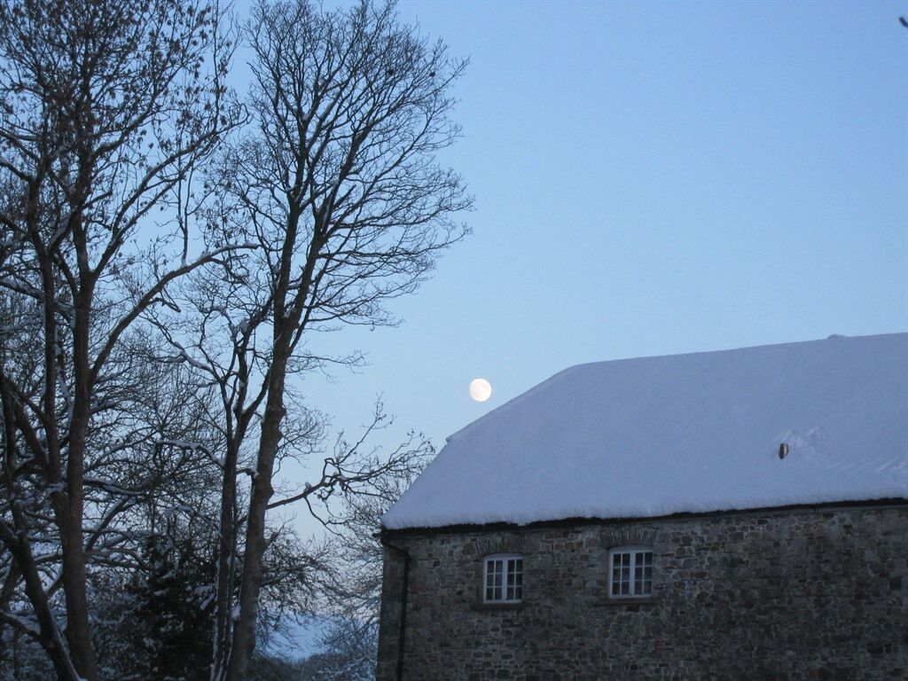 Ein Steinhaus mit schneebedecktem Dach und einem sichtbaren Mond am Himmel.