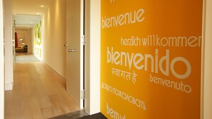 A hallway with a bright orange wall featuring the word "bienvenidos" in multiple languages, leading to a room with a door. - Cosmo Apartments Rambla de Catalunya (Barcelona)
