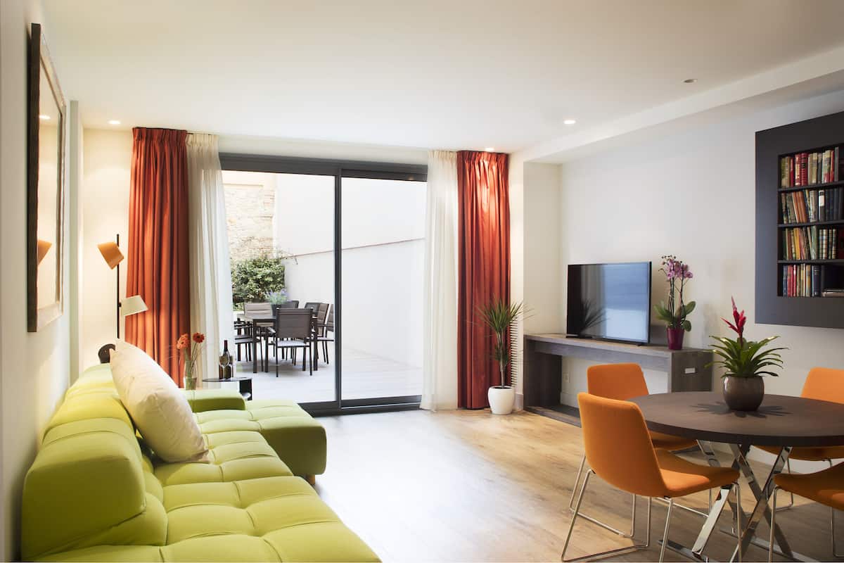 Un salon moderne avec un canapé vert, des fauteuils orange, un téléviseur à écran plat et une bibliothèque.