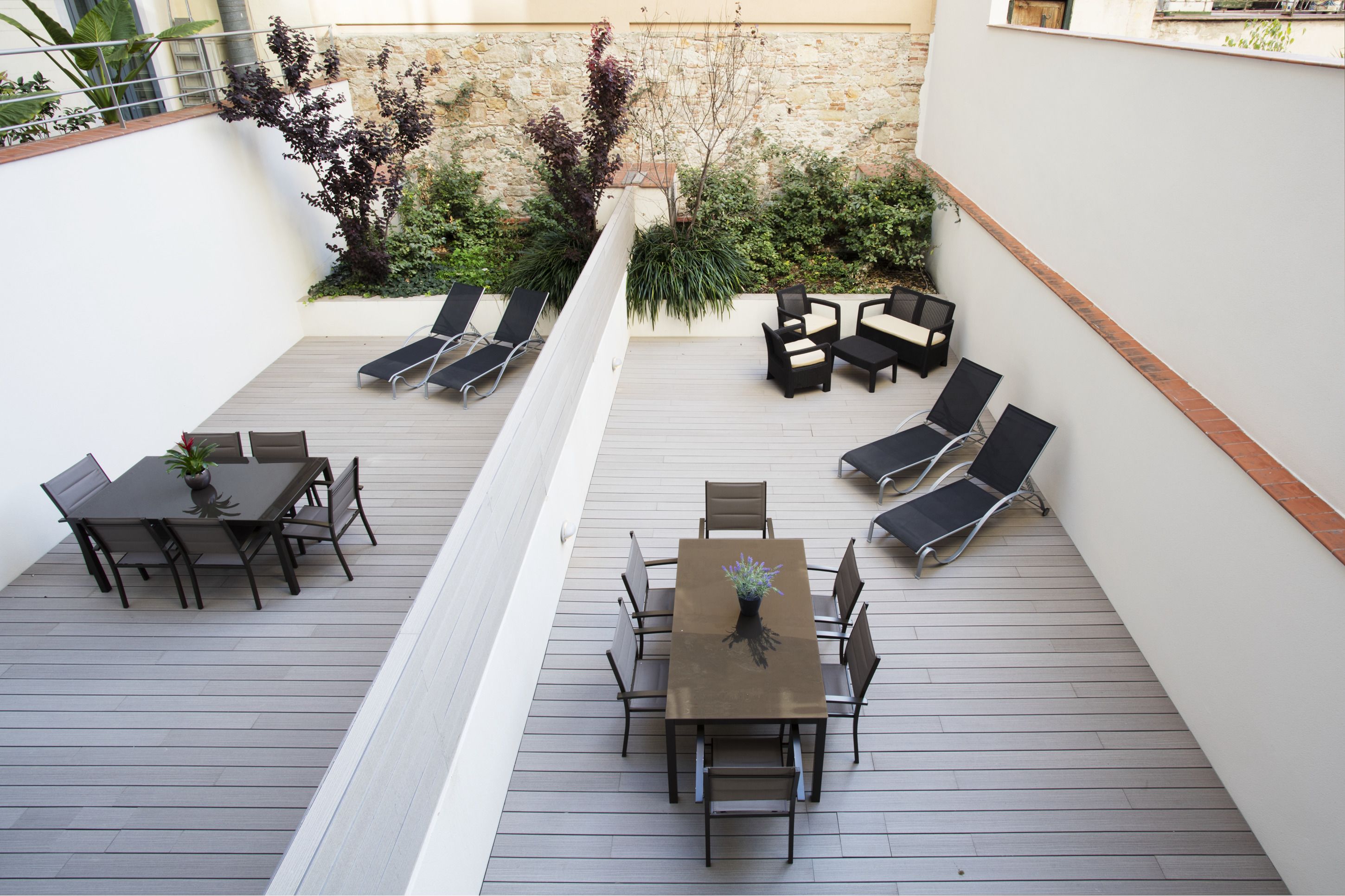 An outdoor patio with a wooden deck, a round table with chairs, and several lounge chairs.