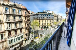 Une vue d’une rue de la ville, avec des immeubles à plusieurs étages, un bâtiment aux lignes courbes portant une enseigne bleue, et un passage piéton.
