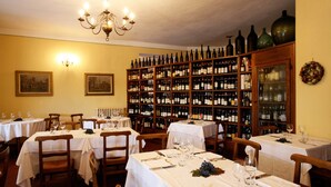 A dining area with tables set for service, a wine cellar with numerous bottles, and a chandelier. - Hotel Barolo (Barolo)