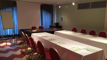 A conference room with a long table, red chairs, a whiteboard, and a projector screen.