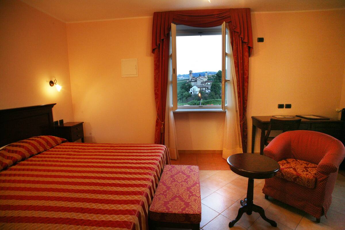 A hotel room with a large bed, a small table, a chair, and a window with curtains.