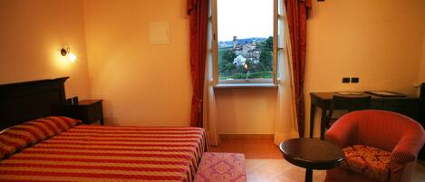Une chambre d’hôtel avec un grand lit, une petite table, une chaise et une fenêtre avec des rideaux.