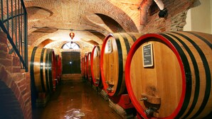 A series of wooden wine barrels in a brick-walled cellar with a herringbone floor pattern. - Hotel Barolo (Barolo)