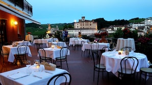 An outdoor dining area with tables set for two, featuring white tablecloths and candle centerpieces. - Hotel Barolo (Barolo)