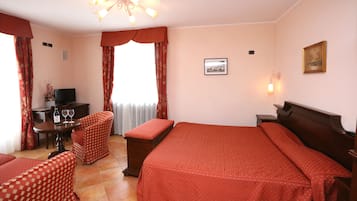 Habitación de hotel con una cama grande, un escritorio con silla, televisión y ventana con cortinas.