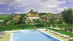 A swimming pool with lounge chairs and a view of historic buildings in the background. - Hotel Barolo (Barolo)
