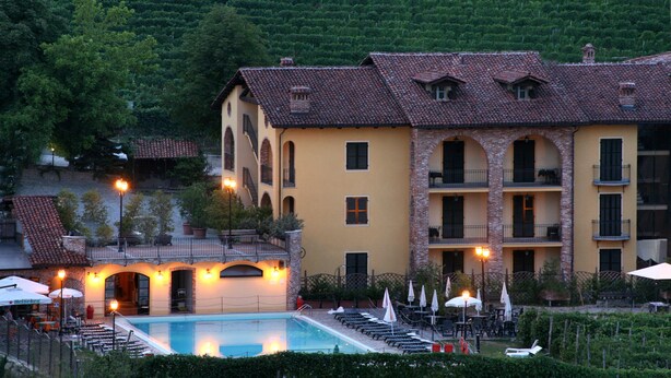 A hotel with a swimming pool, outdoor seating, and a view of a green hillside. - Hotel Barolo (Barolo)