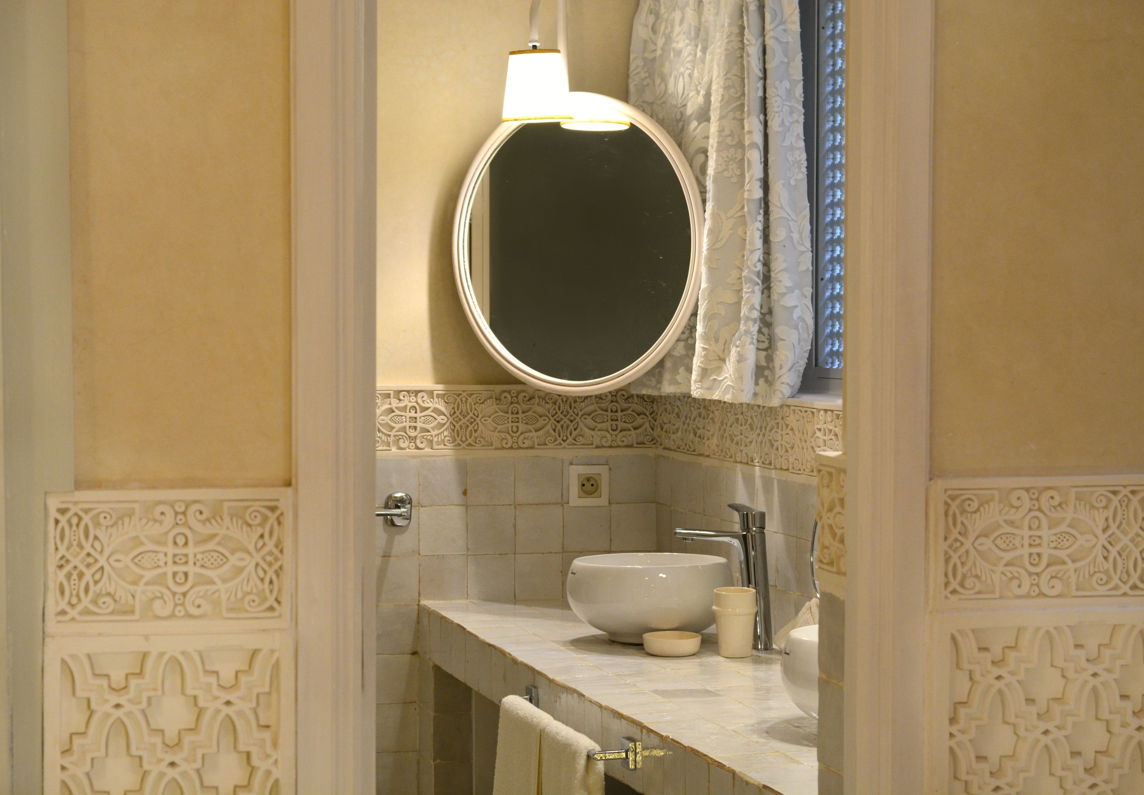 A bathroom with a round mirror, a sink, and a towel rack.