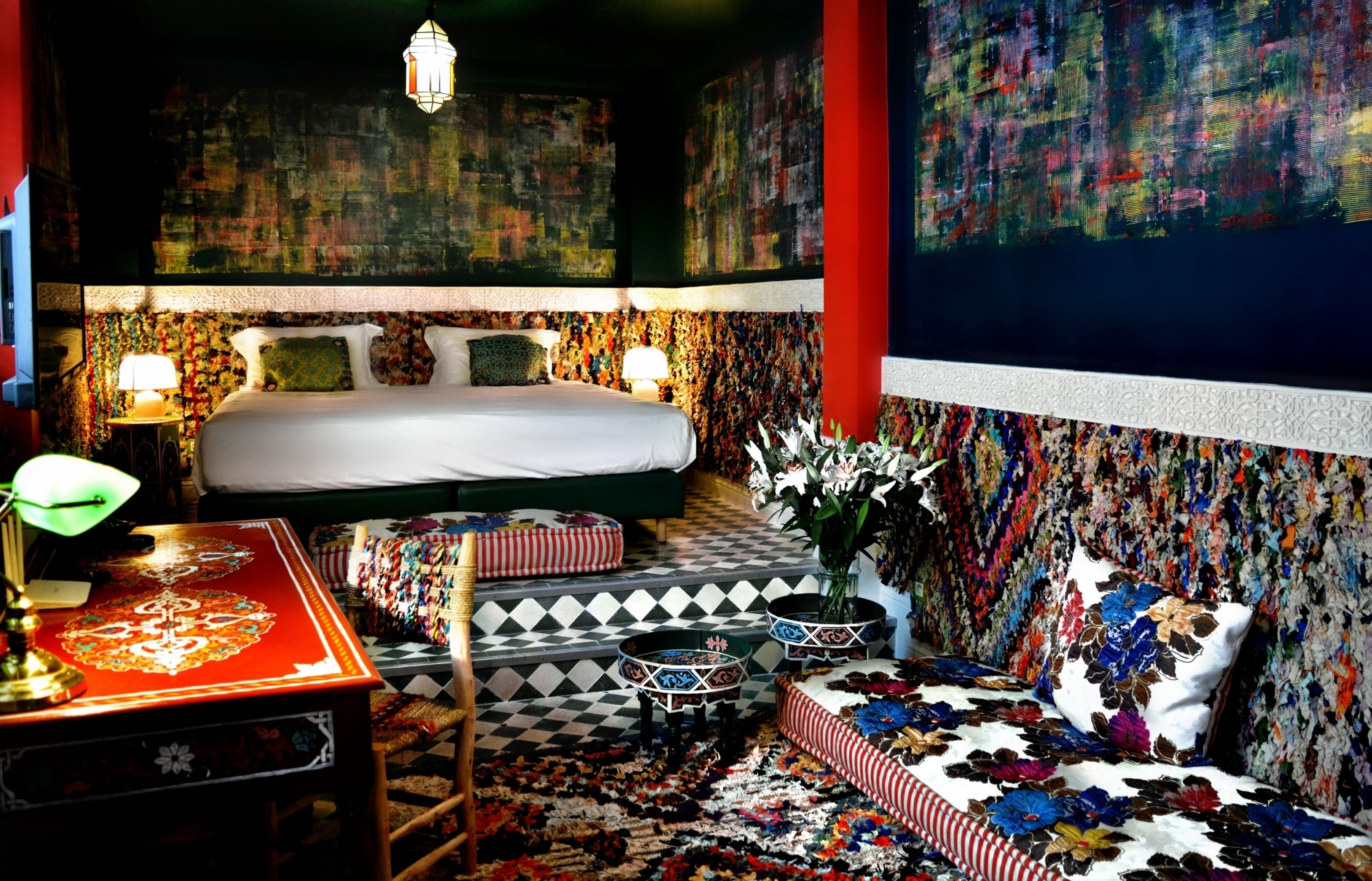 Een slaapkamer met een bed, nachtkastje, lamp, een kamerbreed tapijt met patroon en een muur met abstracte kunst.