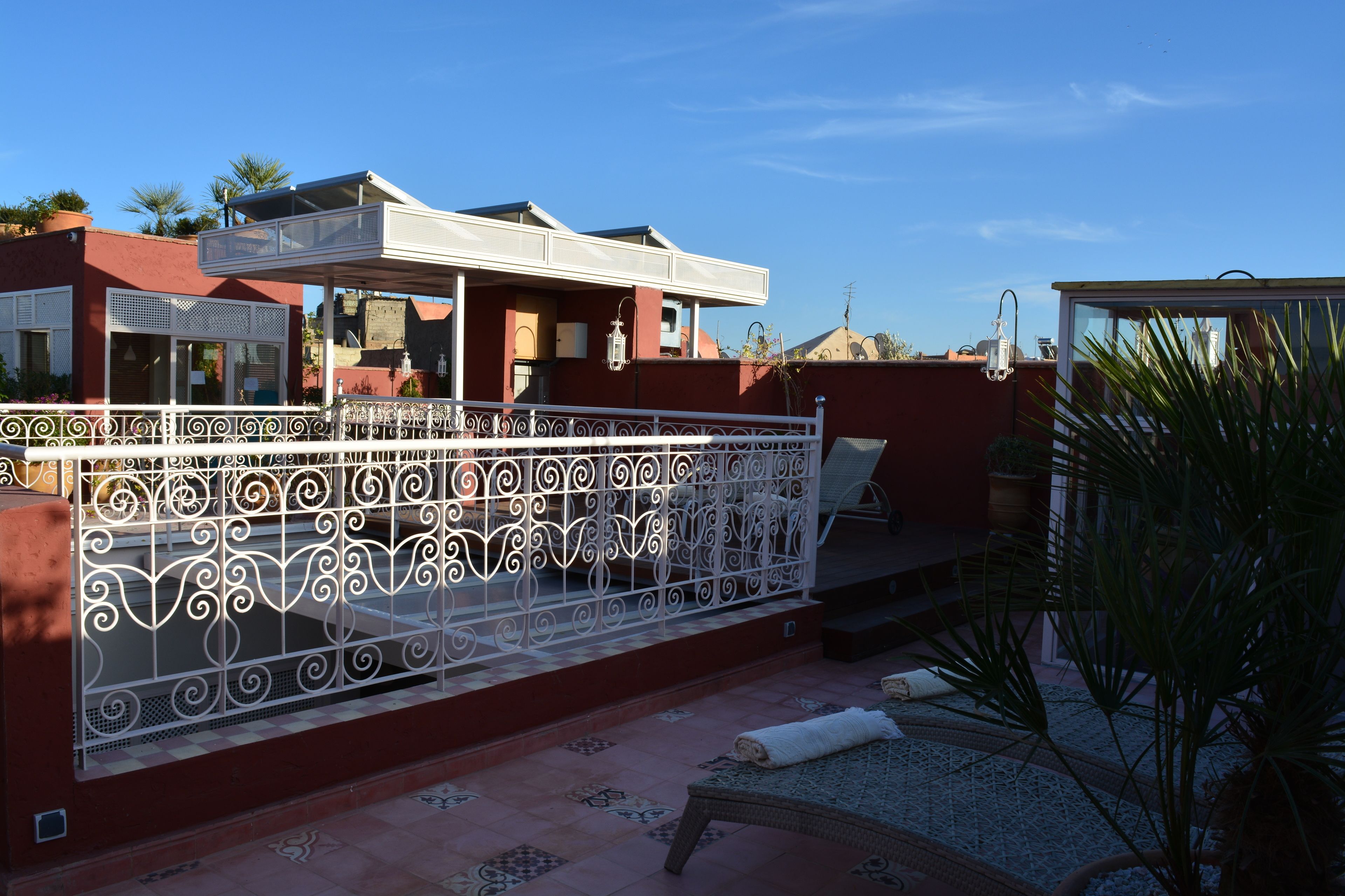 A rooftop terrace with a decorative white metal fence, a covered seating area, and a small garden with a palm tree.