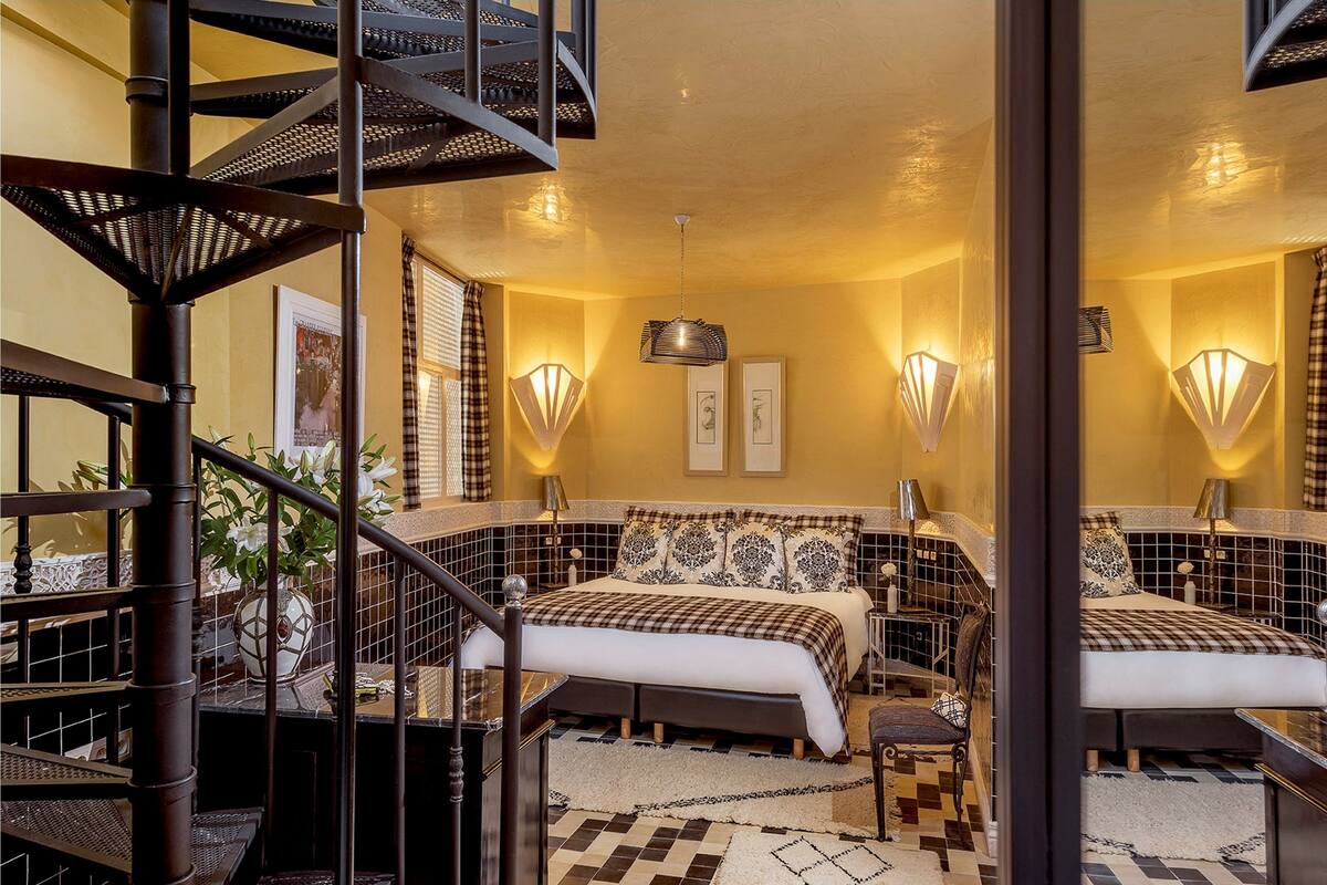 A bedroom with a checkered bedspread, a black metal spiral staircase, and wall-mounted lamps.