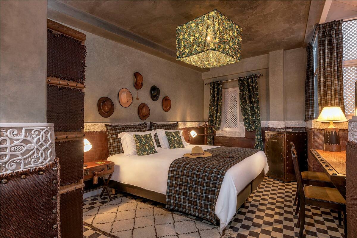 A hotel room with a checkered floor, a bed with a plaid bedspread, a decorative wall with wooden and metal elements, and a hanging light fixture.