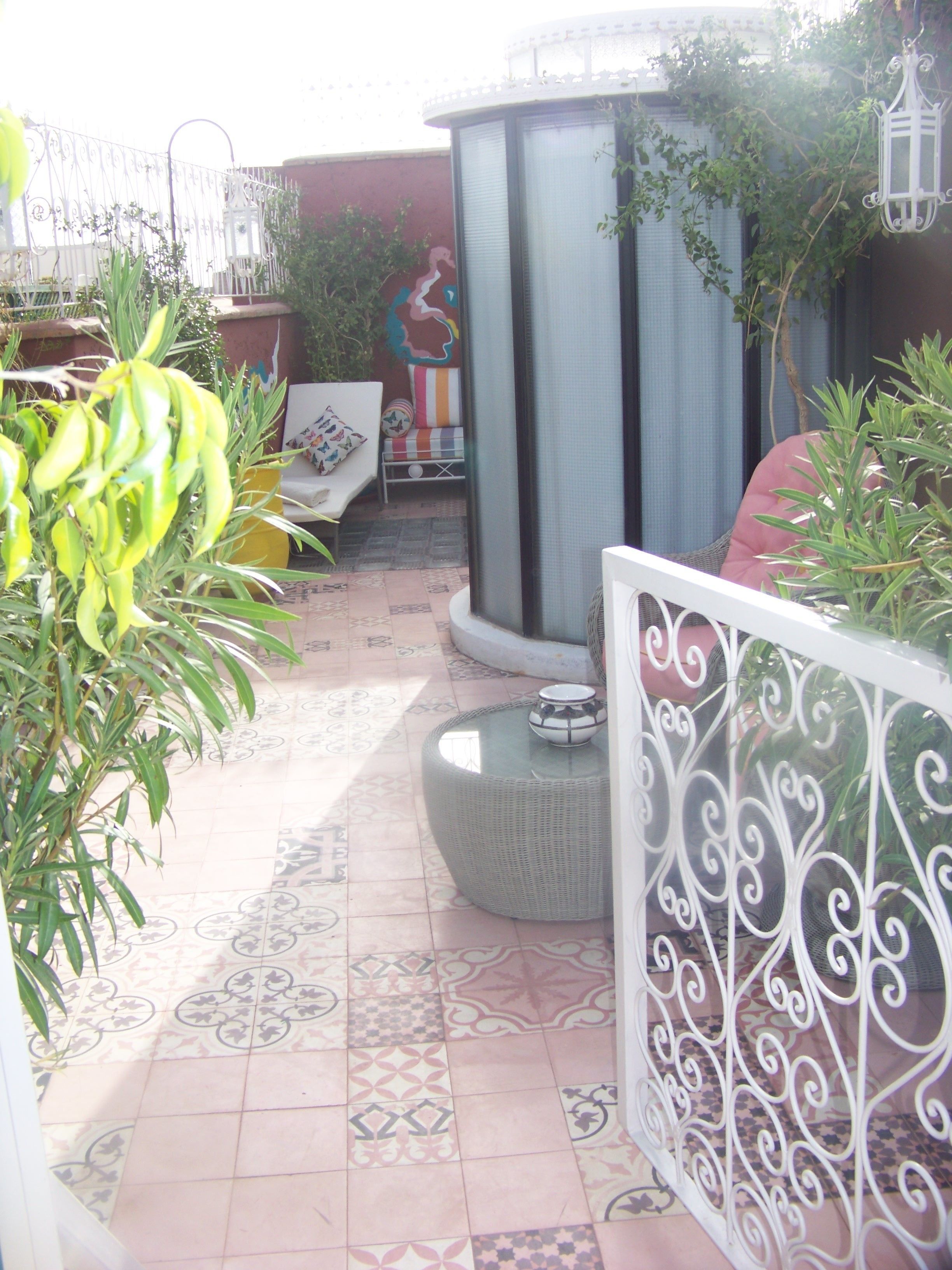 A tiled patio with a decorative fence, a seating area with cushions, and a potted plant.