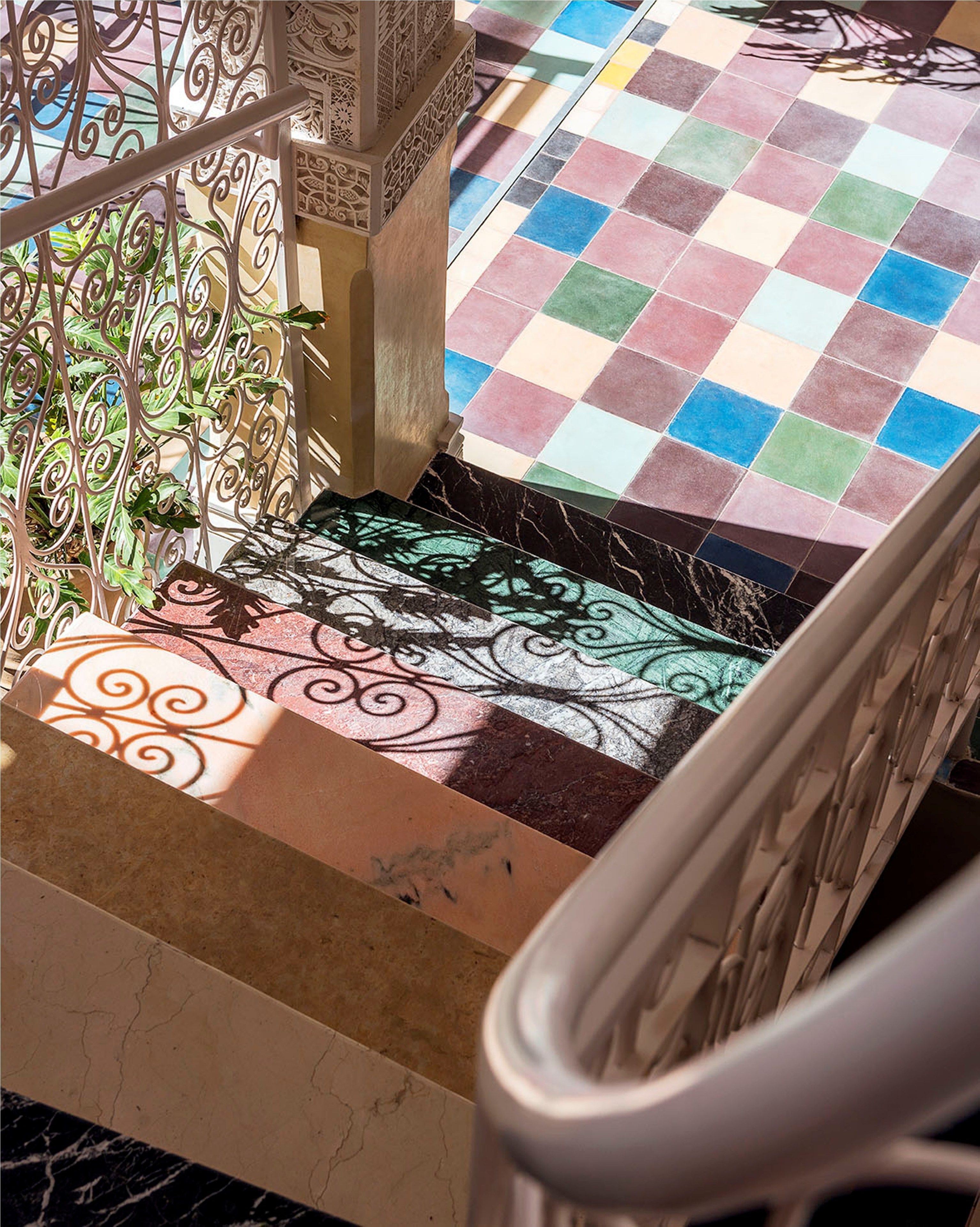 Un escalier dont le sol présente un motif à carreaux, avec une rampe en métal et des éléments décoratifs en métal.