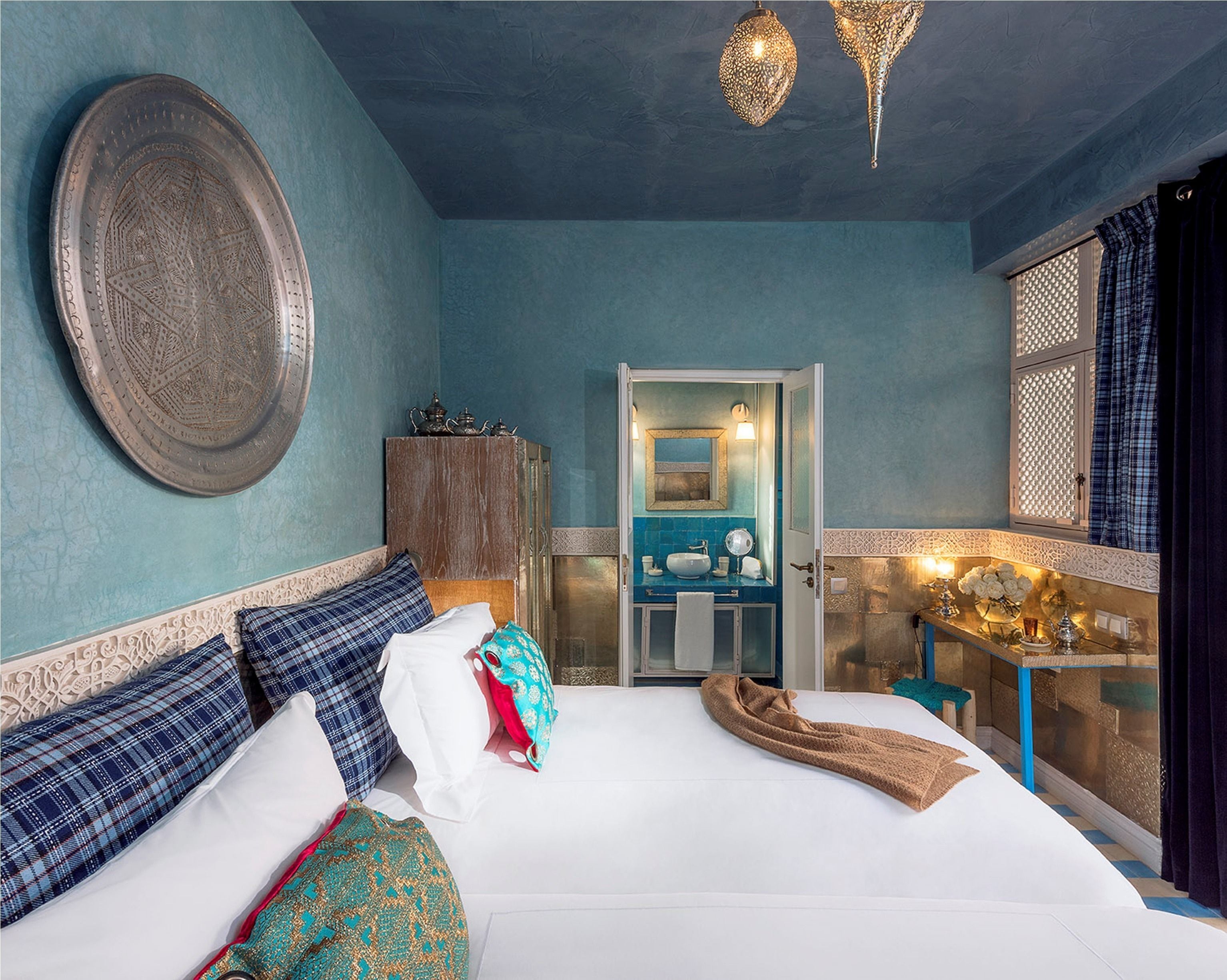 Quarto com cama grande, armário, banheiro com pia e espelho, e luminária decorativa no teto.