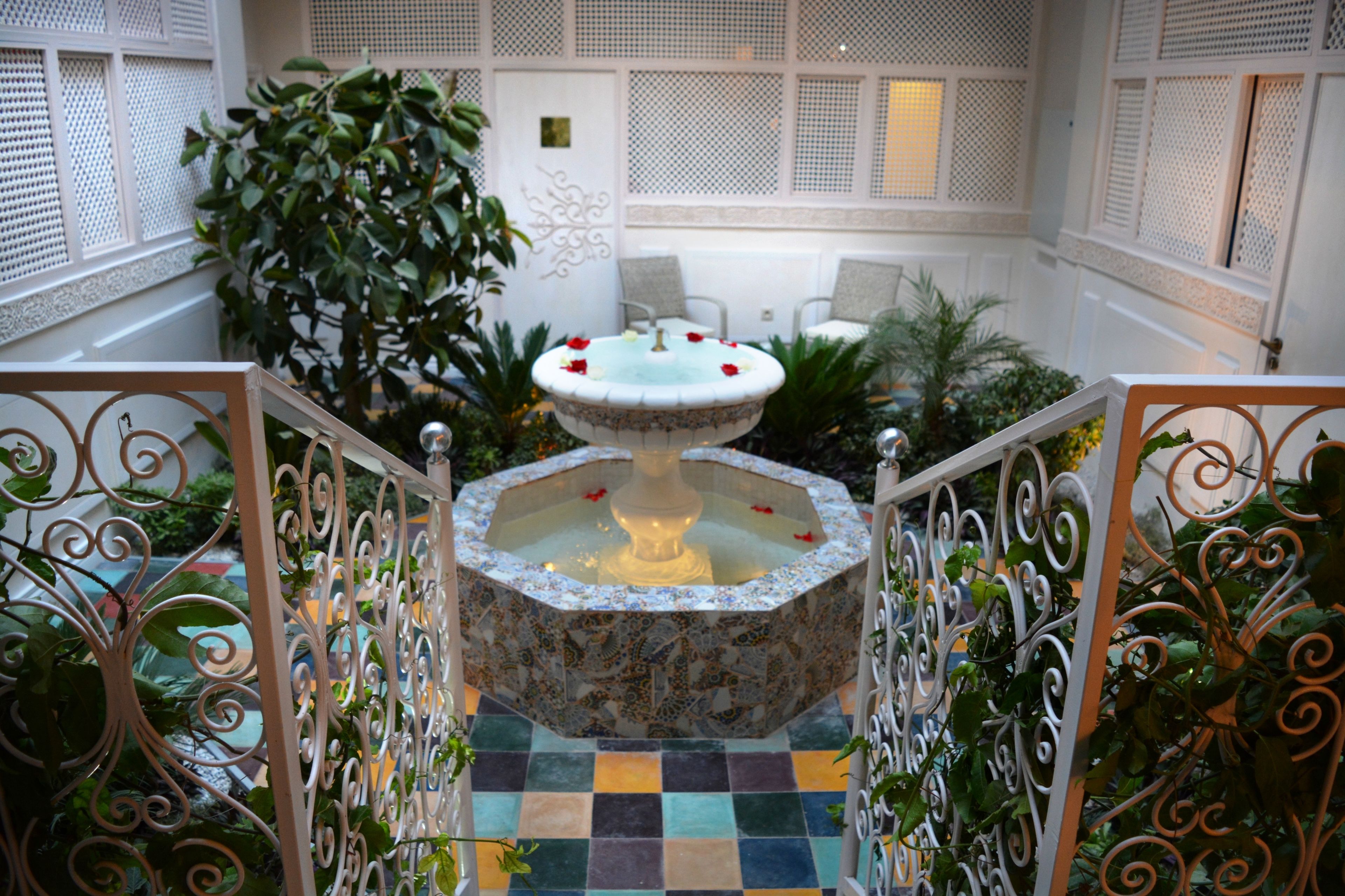 A courtyard with a decorative fountain, potted plants, and a seating area with chairs.