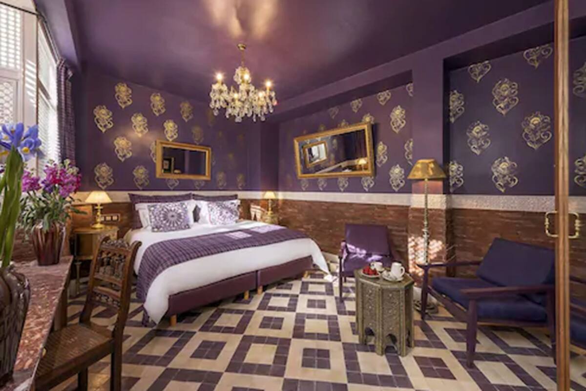 A bedroom with a large bed, a chandelier, a mirror, and a seating area with a chair and a small table.