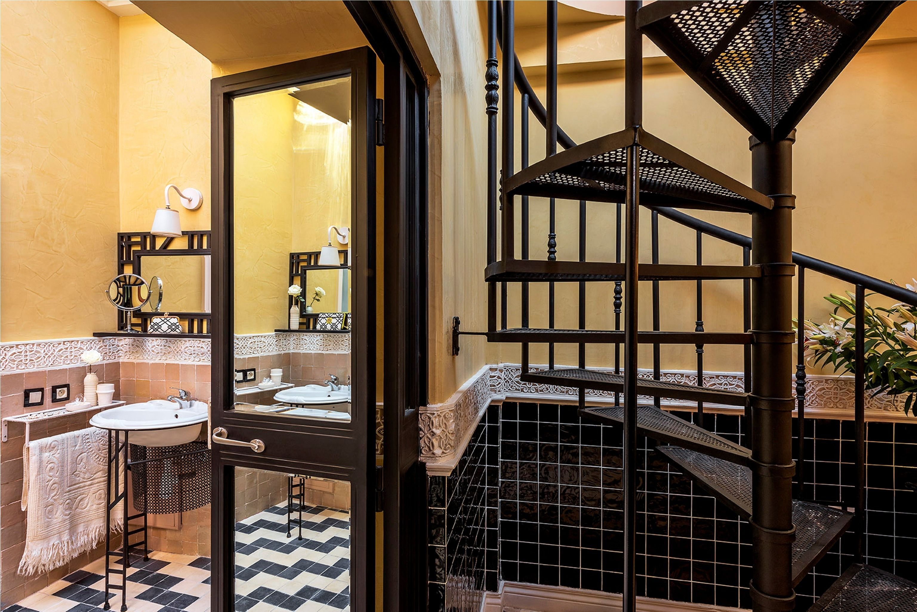 A bathroom with a black and white checkered floor, a sink, a mirror, and a staircase with a black metal railing.