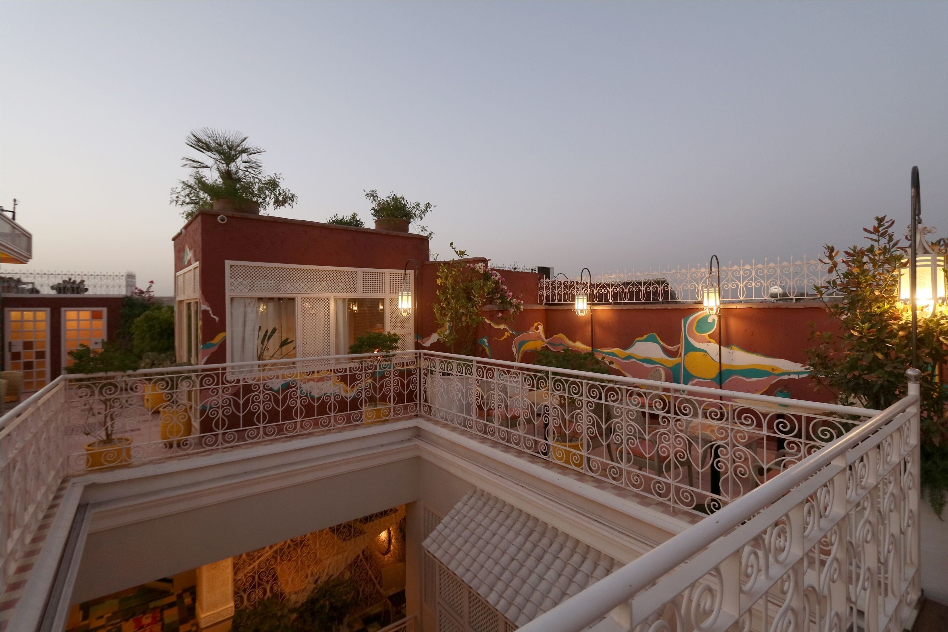 A multi-level building with ornate white railings, a balcony with potted plants, and a mural on the upper level.