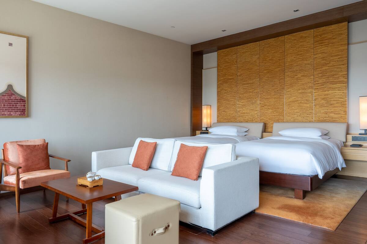 A hotel room with a sofa, a chair, a small table, a bed, and a nightstand.