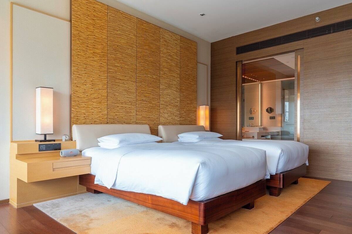 A modern hotel room with a large bed, wooden headboard, bedside tables, and a large mirror.