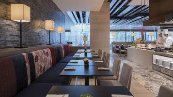 Um restaurante moderno com mesas comunitárias grandes, uma parede de tijolos e vista para a cidade.