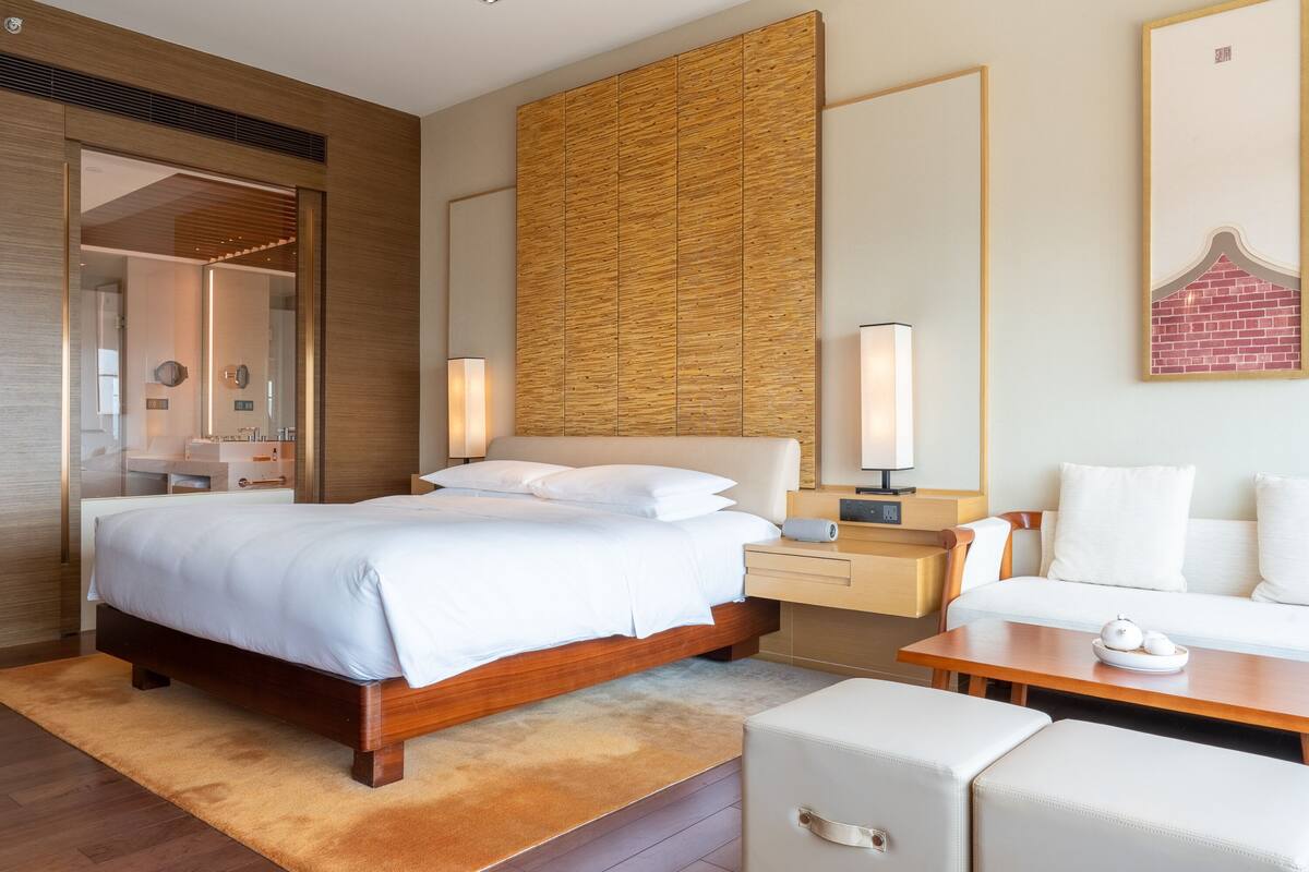 A modern hotel room with a large bed, bedside tables, a seating area, and a wooden accent wall.