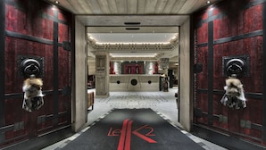 A hallway with a red carpet leading to a reception area, flanked by wooden doors with fur decorations. - Hôtel Le K2 Altitude (Courchevel)