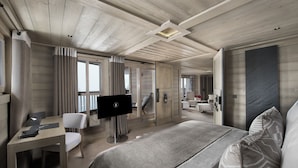 A modern hotel room with a large bed, a desk, a TV, and a balcony with curtains. - Hôtel Le K2 Altitude (Courchevel)