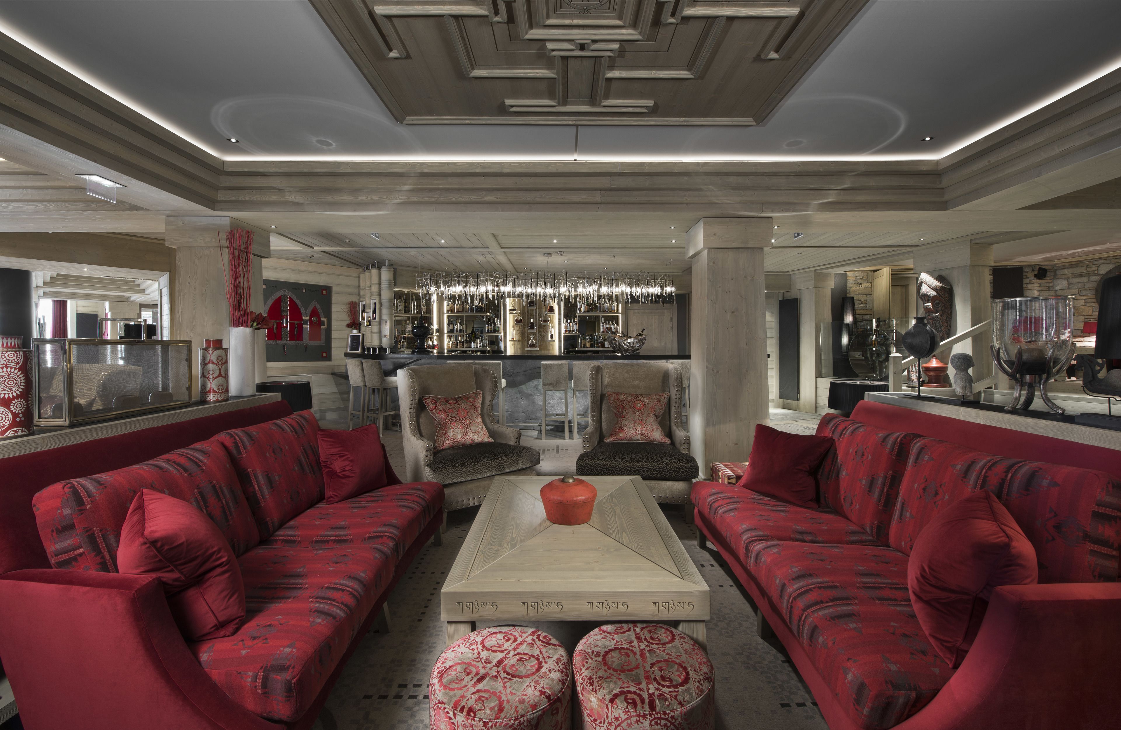 A spacious living area with a central coffee table, red sofas, and a bar area in the background.