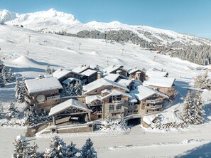 A snow-covered lodge with multiple buildings, ski slopes, and a ski lift in the background. - Hôtel Le K2 Altitude (Courchevel)