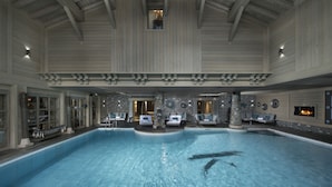 An indoor swimming pool with stone pillars, lounge chairs, and a stone wall with a fireplace. - Hôtel Le K2 Altitude (Courchevel)