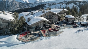 A snow-covered lodge with a ski lift, outdoor seating, and a view of snow-capped mountains. - Hôtel Le K2 Altitude (Courchevel)