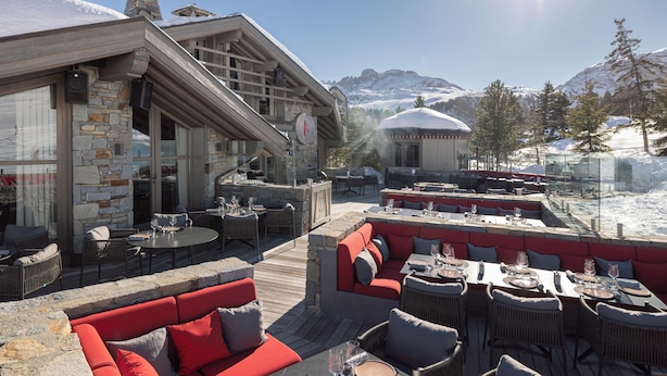 A restaurant with outdoor seating, stone walls, and a view of snow-covered mountains. - Hôtel Le K2 Altitude (Courchevel)