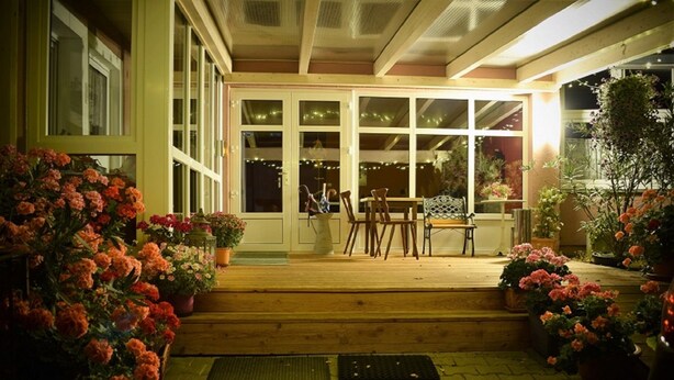 A wooden porch with a table and chairs, surrounded by potted plants and flowers. - Wellnesshaus Waldmunchen (Waldmuenchen)