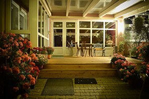 A wooden porch with a table and chairs, surrounded by potted plants and flowers. - Wellnesshaus Waldmunchen (Waldmuenchen)