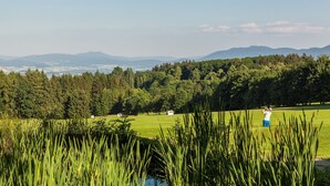 A golf course with a person in the distance, surrounded by lush greenery and distant mountains. - Wellnesshaus Waldmunchen (Waldmuenchen)