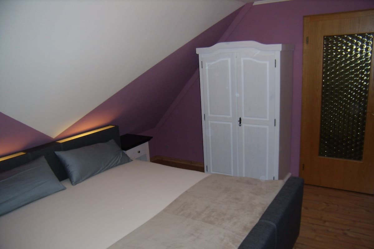 Un dormitorio con cama, mesitas de noche, armario y puerta con panel de vidrio texturizado.