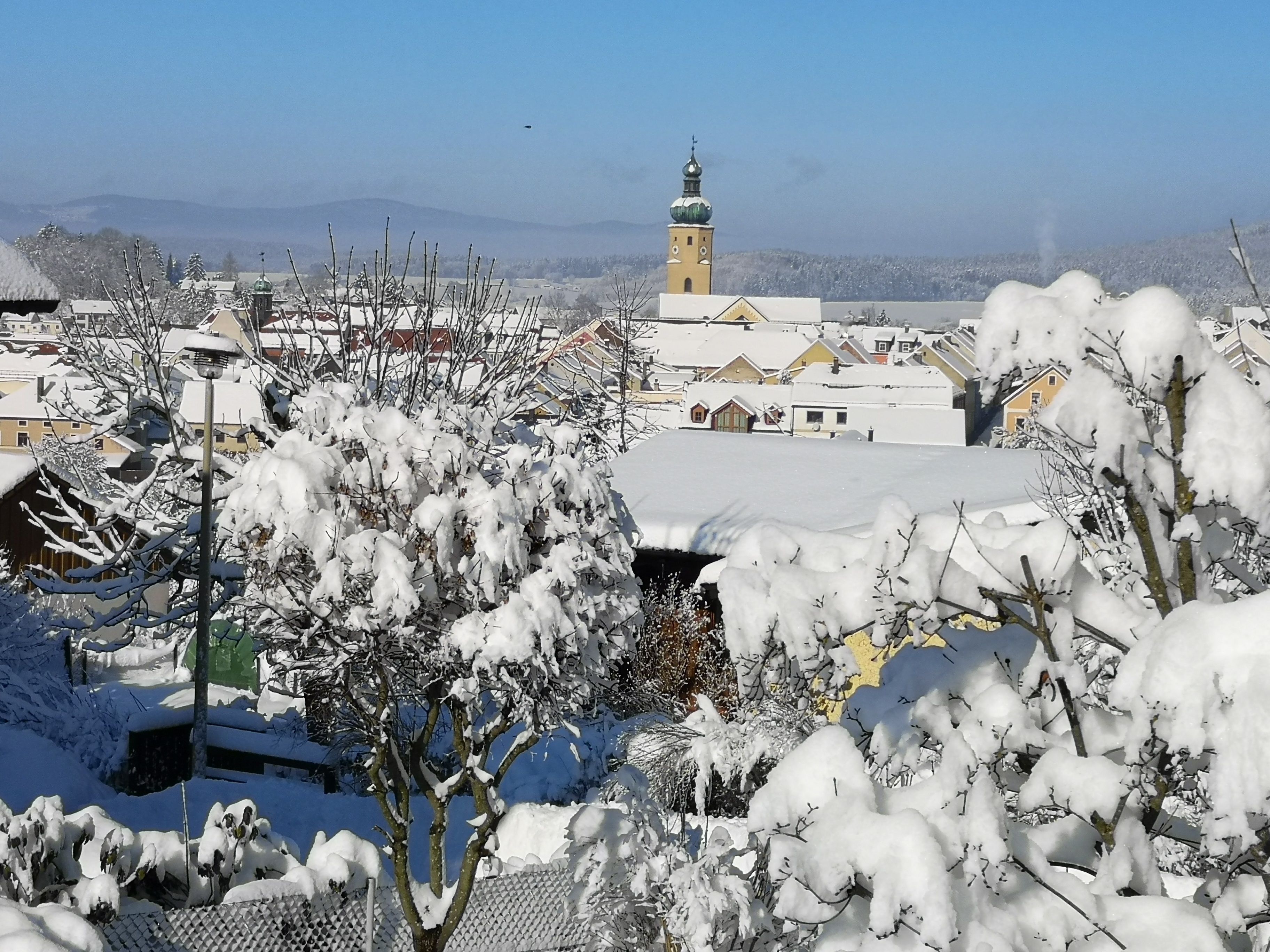 A snow-covered town with a prominent church tower, residential buildings, and a clear sky.