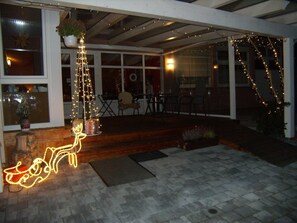 Un espacio al aire libre cubierto con un banco de madera, un árbol de Navidad y luces colgantes.