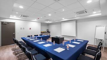 Un salón de conferencias con una larga mesa, sillas, una pantalla de proyector y una pizarra.