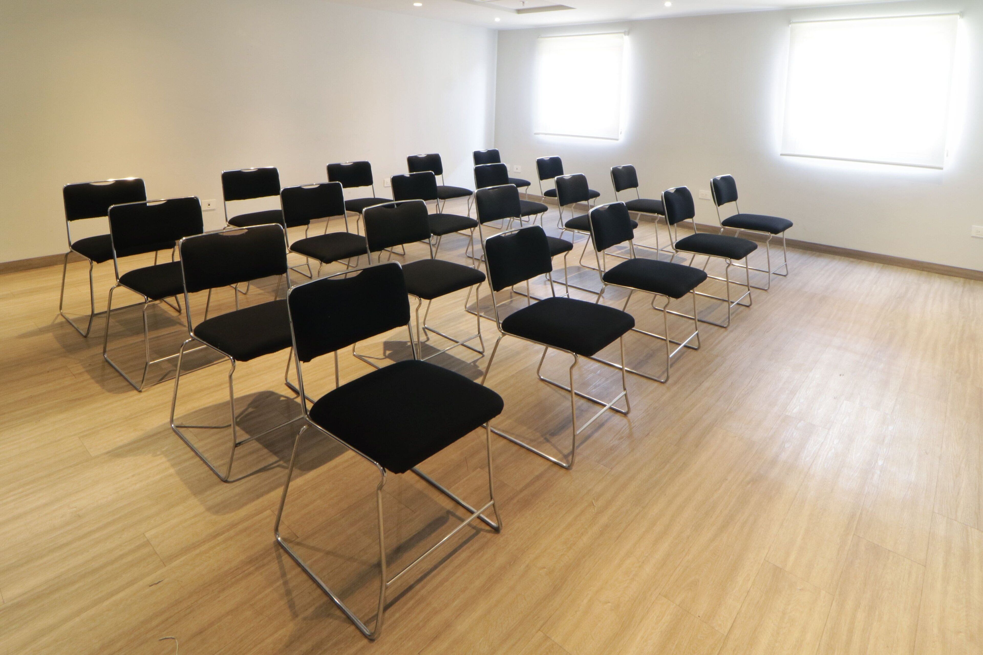 A conference room with rows of black chairs and a wooden floor.