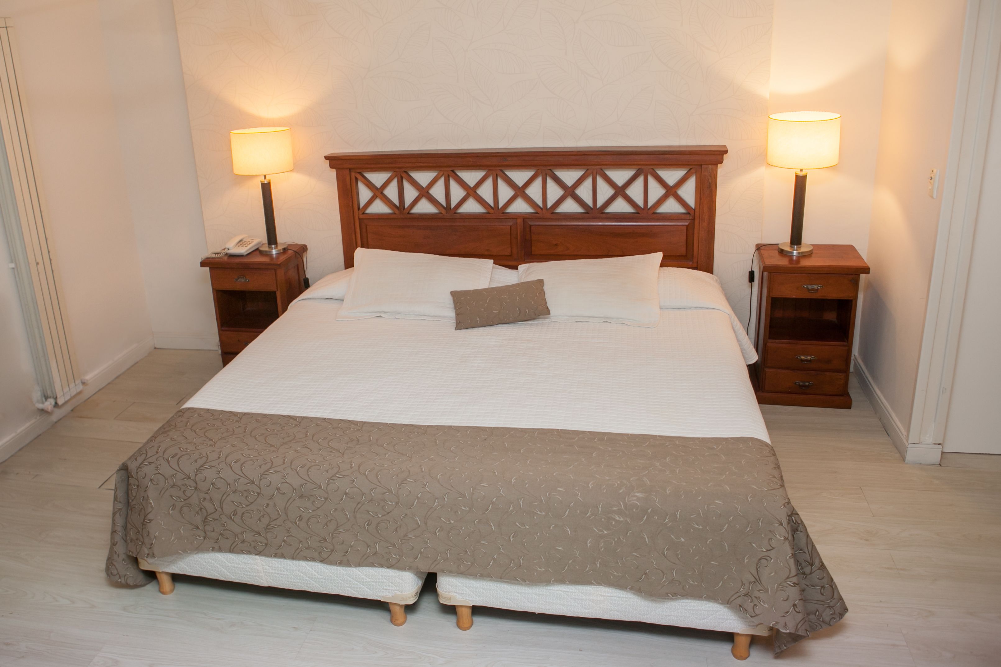 A neatly made bed with a wooden headboard, two bedside tables with lamps, and a bedside phone.