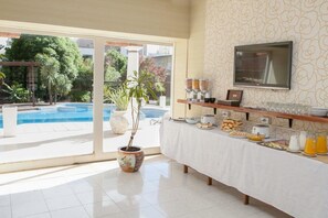 Un bufé de desayuno con vista a la piscina, un televisor y una planta al frente.