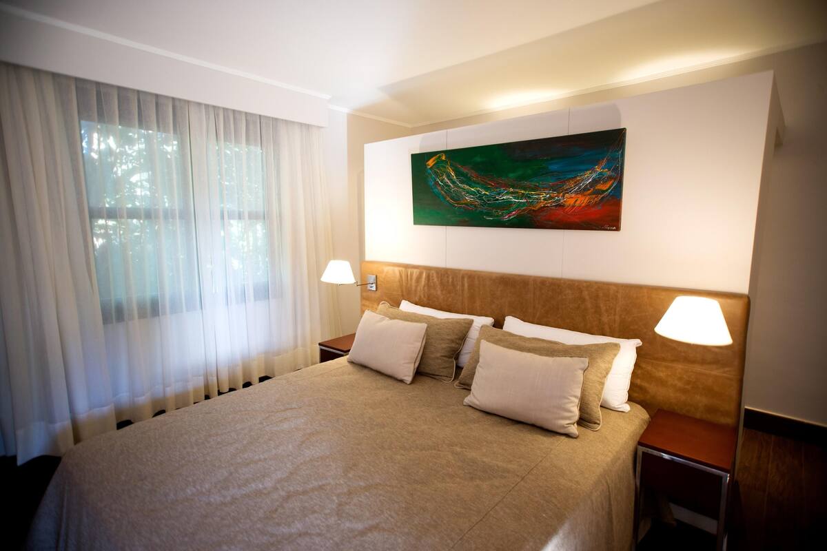 Ein Hotelzimmer mit einem großen Bett, zwei Nachttischlampen, einem Bild an der Wand und transparenten Vorhängen.